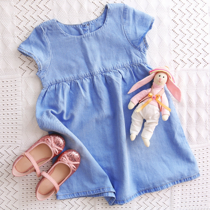 Blue dress with pink shoes and a stuffed bunny on a textured white surface