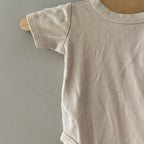 Close-up detail of Goumi x Babylist natural cream organic cotton short-sleeve baby bodysuit showing soft fabric and sleeve stitching size 6-9 months