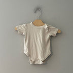 Front view of Goumi x Babylist cream organic cotton gender neutral short-sleeve bodysuit with shoulder snap and snap closure size 6-9 months