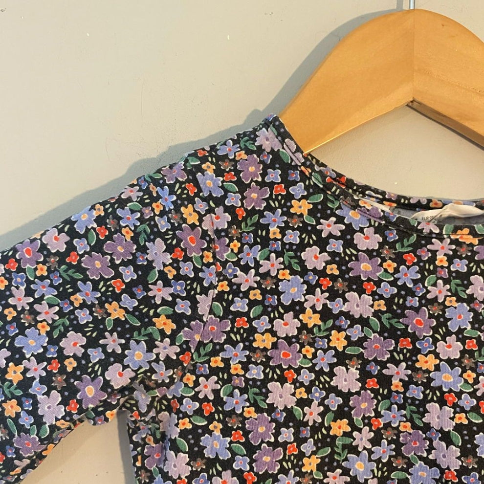 Close-up detail of H&M black long-sleeve girls dress showing multicolor ditsy floral print in purple orange and blue flowers, size 3Y