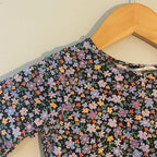 Close-up detail of H&M black long-sleeve girls dress showing multicolor ditsy floral print in purple orange and blue flowers, size 3Y