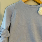 Close-up detail of Janie and Jack blue sweater showing knit texture, tiered ruffle sleeves and white rosette accent