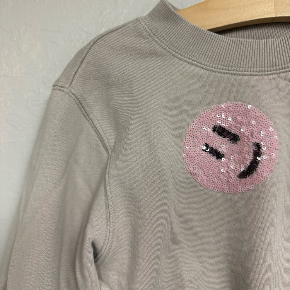Close-up of a pink sequin smiley face patch on a Molo light gray girls’ sweatshirt in size 6Y (EU 116).