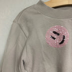 Close-up of a pink sequin smiley face patch on a Molo light gray girls’ sweatshirt in size 6Y (EU 116).