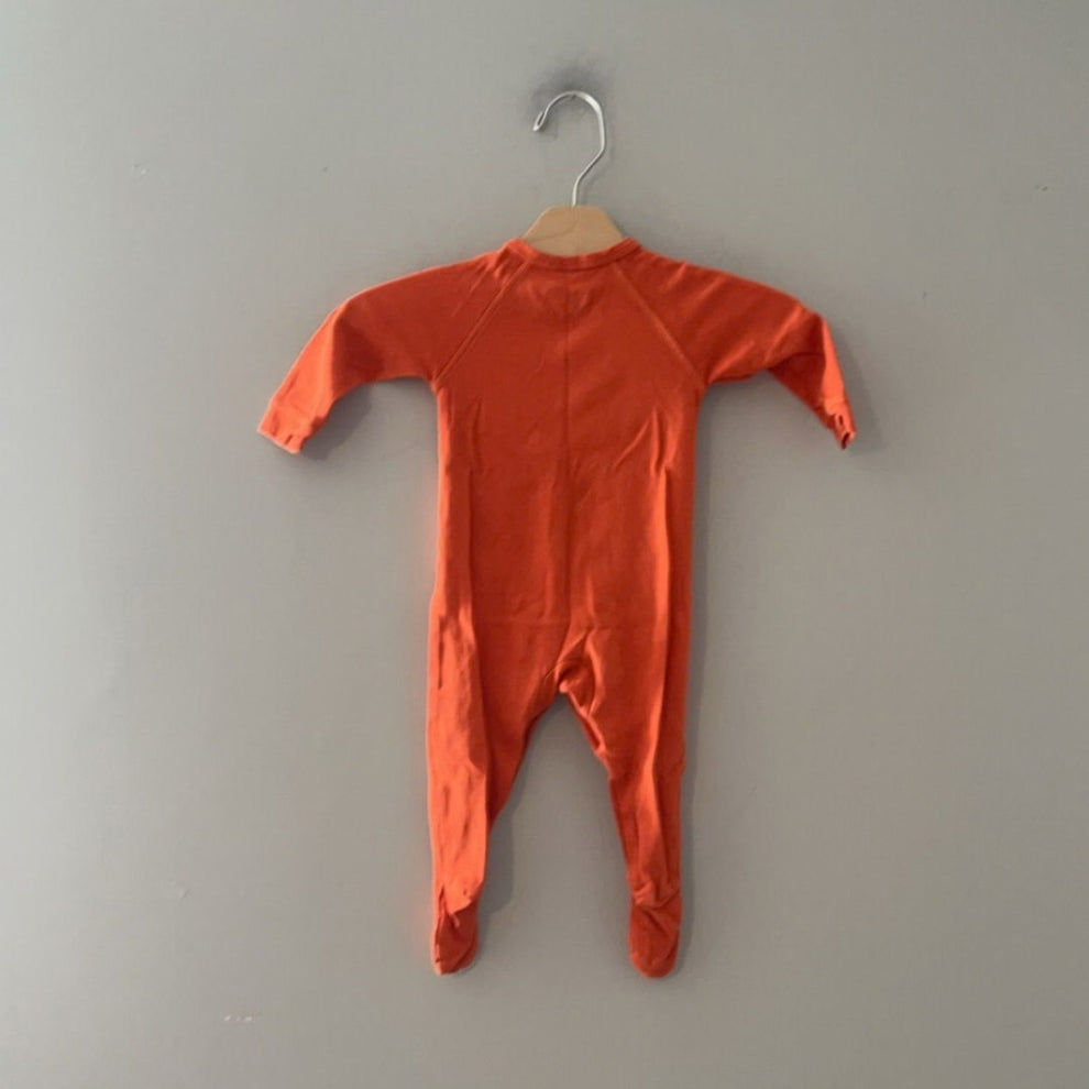 Back view of a Primary orange organic cotton footie sleeper, size 0–3 months, showing the smooth back and raglan sleeve seams.