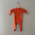 Back view of a Primary orange organic cotton footie sleeper, size 0–3 months, showing the smooth back and raglan sleeve seams.