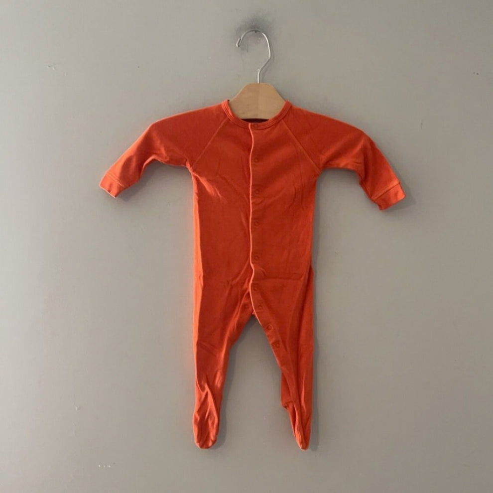 Front view of a Primary organic cotton orange unisex footed sleeper in size 0–3 months with snap-button front and long sleeves.