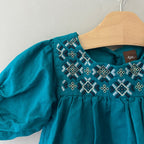 Close-up detail of Tea Collection jade green dress showing geometric cross-stitch embroidery in navy white and gold on yoke collar