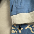 Close-up detail of Tiny Tribe Australia label on blue jogger pants waistband and white ribbed hem of matching sweatshirt, size 3Y